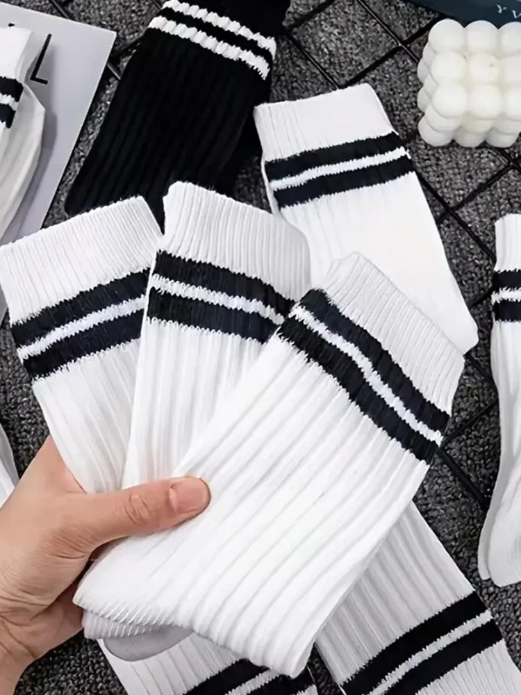A hand holds a stack of white and black striped men's socks on a dark textured surface.