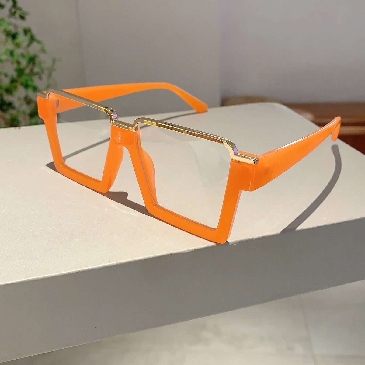 Orange square semi-rim metal eyeglasses resting on a white surface.
