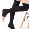 A person wearing black compression thigh high socks sitting on a white stool.