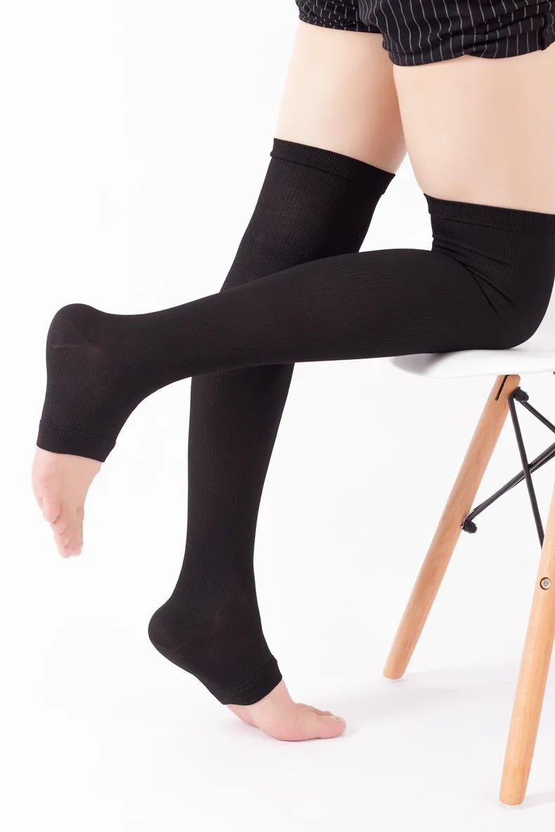 A person wearing black compression thigh high socks sitting on a white stool.