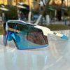A pair of blue-tinted sports sunglasses with white frames resting on a reflective surface.