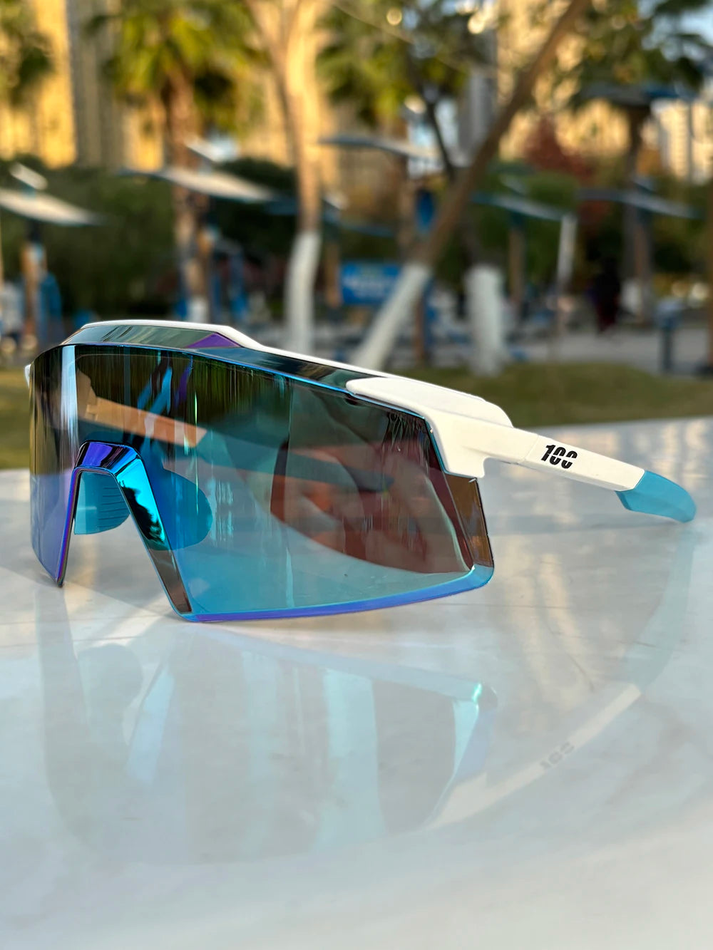 A pair of blue-tinted sports sunglasses with white frames resting on a reflective surface.