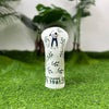 A white golf club head cover featuring a silhouette of a golfer and the year 1961, resting on green grass.