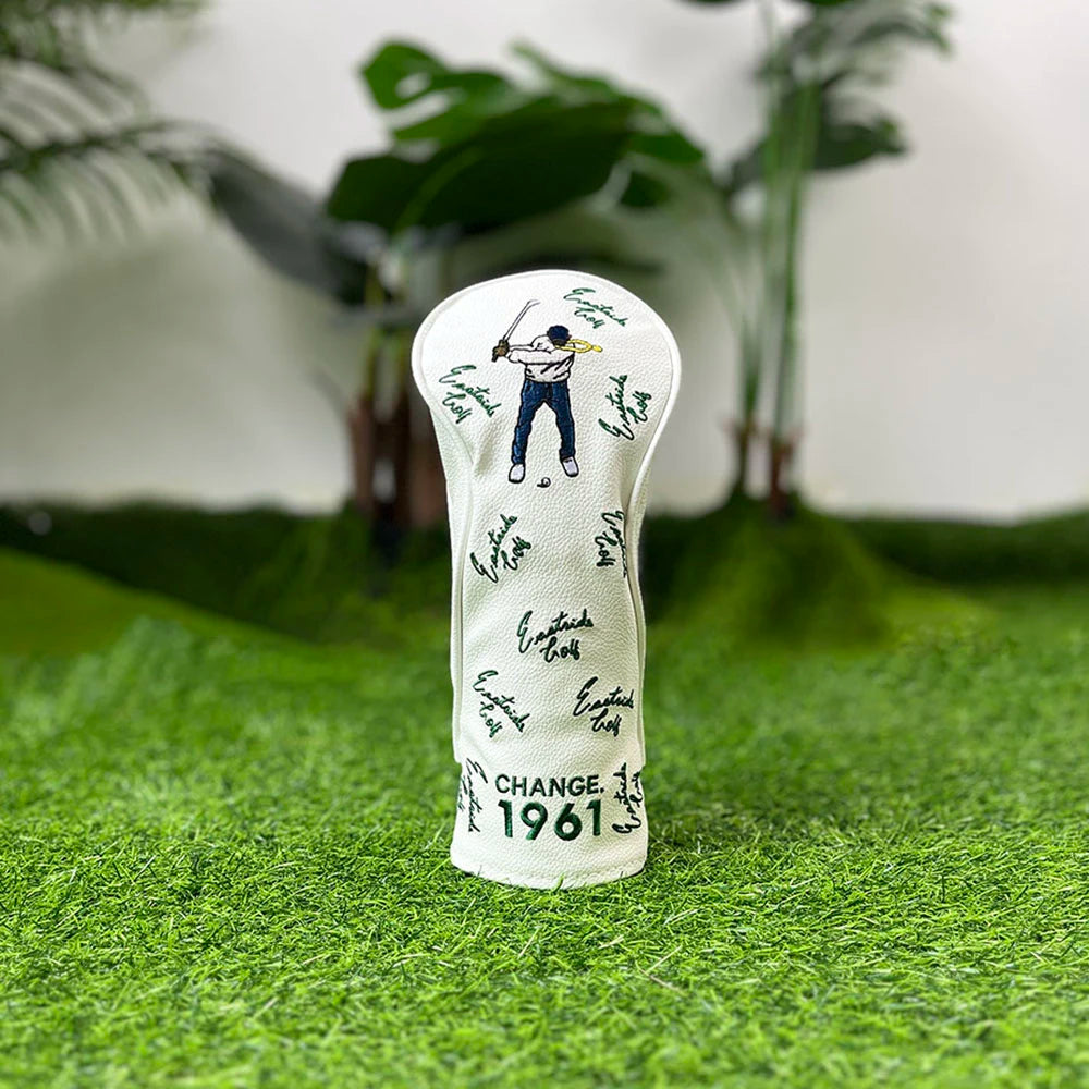 A white golf club head cover featuring a silhouette of a golfer and the year 1961, resting on green grass.