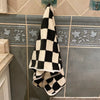 A black and cream checkered face towel hanging on a tiled wall.