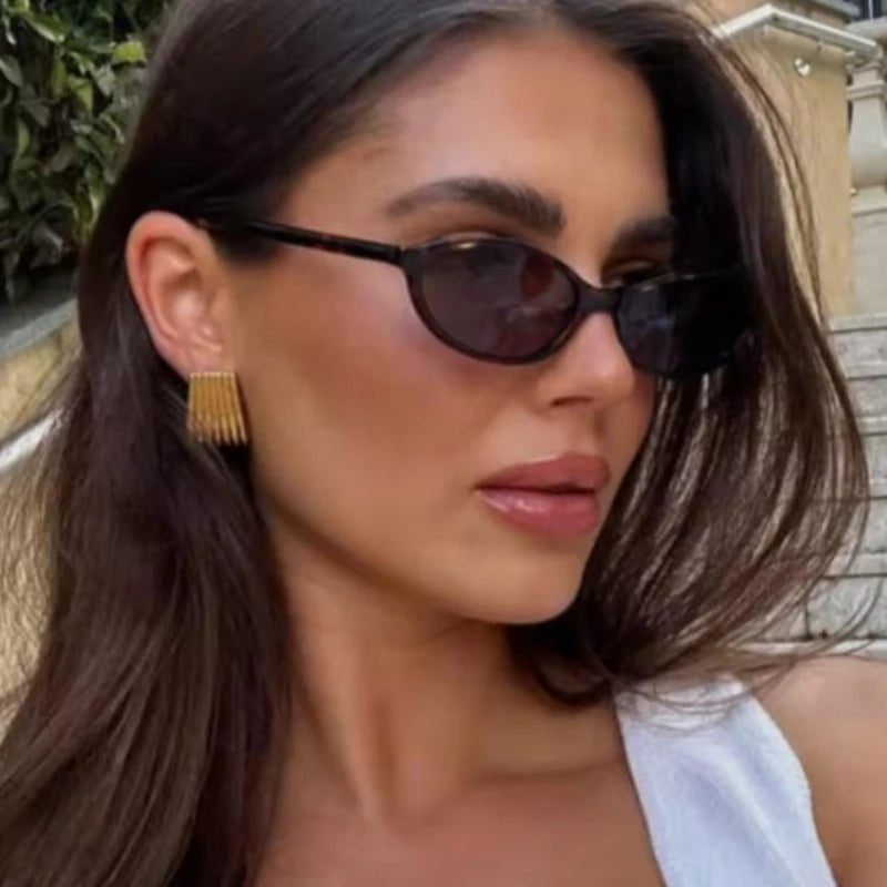 A woman wearing dark retro oval frame sunglasses with long brown hair.