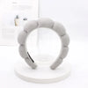 A gray sponge terry cloth headband for hair styling displayed on a white circular stand.