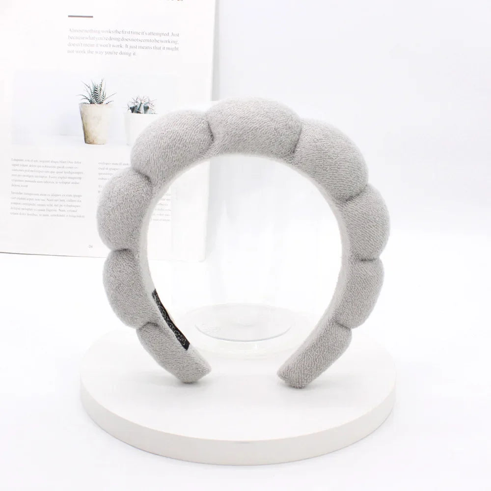 A gray sponge terry cloth headband for hair styling displayed on a white circular stand.