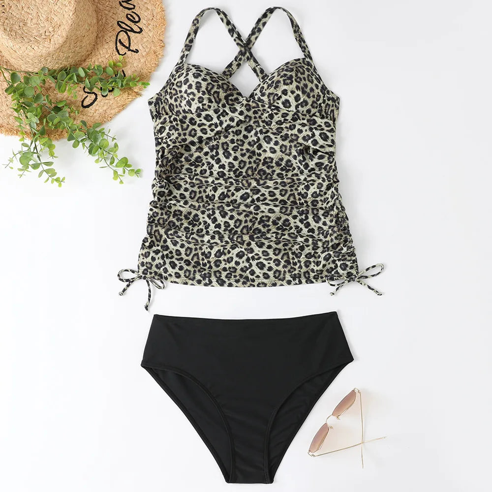 A black leopard print high-waisted two-piece swimsuit set laid out next to a straw hat and green foliage.