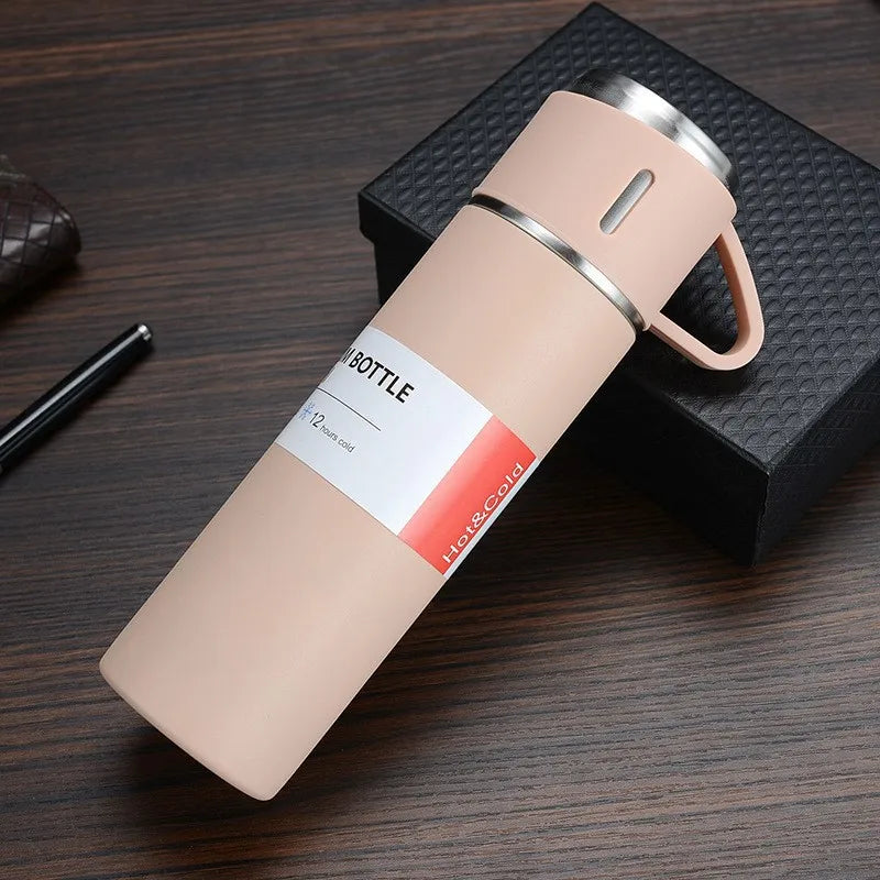 A light pink stainless steel vacuum flask with a silver lid and handle resting on a dark wooden surface.