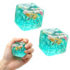 A hand holds a translucent teal squishy stress relief fidget cube filled with colorful, squishy objects.