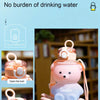 A pink bear-shaped water bottle with a lid and strap is shown being held by a hand.