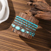 Une pile de cinq bracelets perlés avec des pierres turquoise et du fil d'argent, posés sur un morceau de bois.