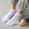 A pair of white thin ankle socks worn by a person, paired with gray pants.