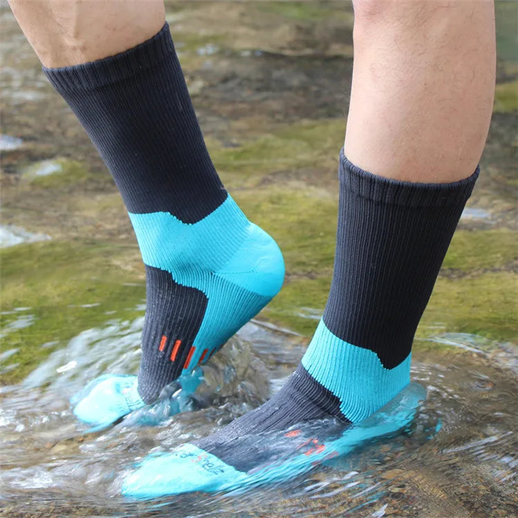 A person wearing waterproof breathable hiking socks with black and light blue accents wading in shallow water.