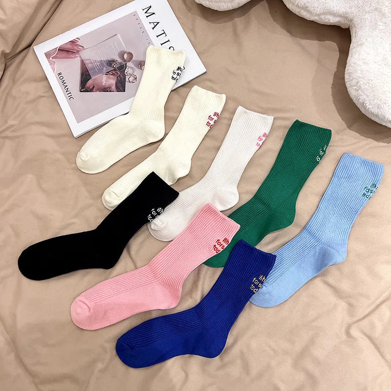 A collection of elegant embroidered cotton socks in various colors including cream, black, pink, and blue, laid out on a beig