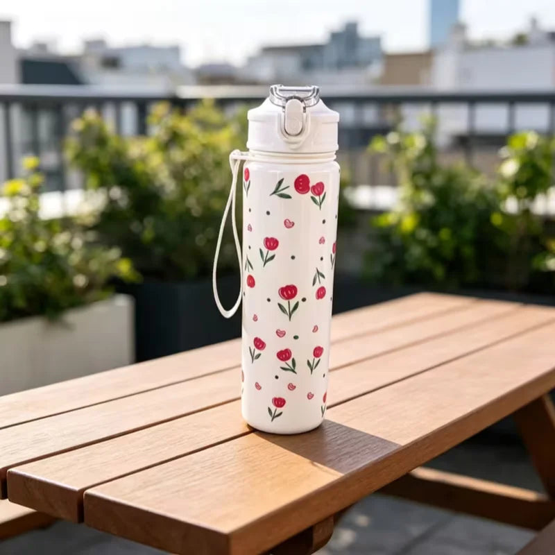 A white tumbler decorated with red strawberry and cherry flowers sits on a wooden table outdoors.