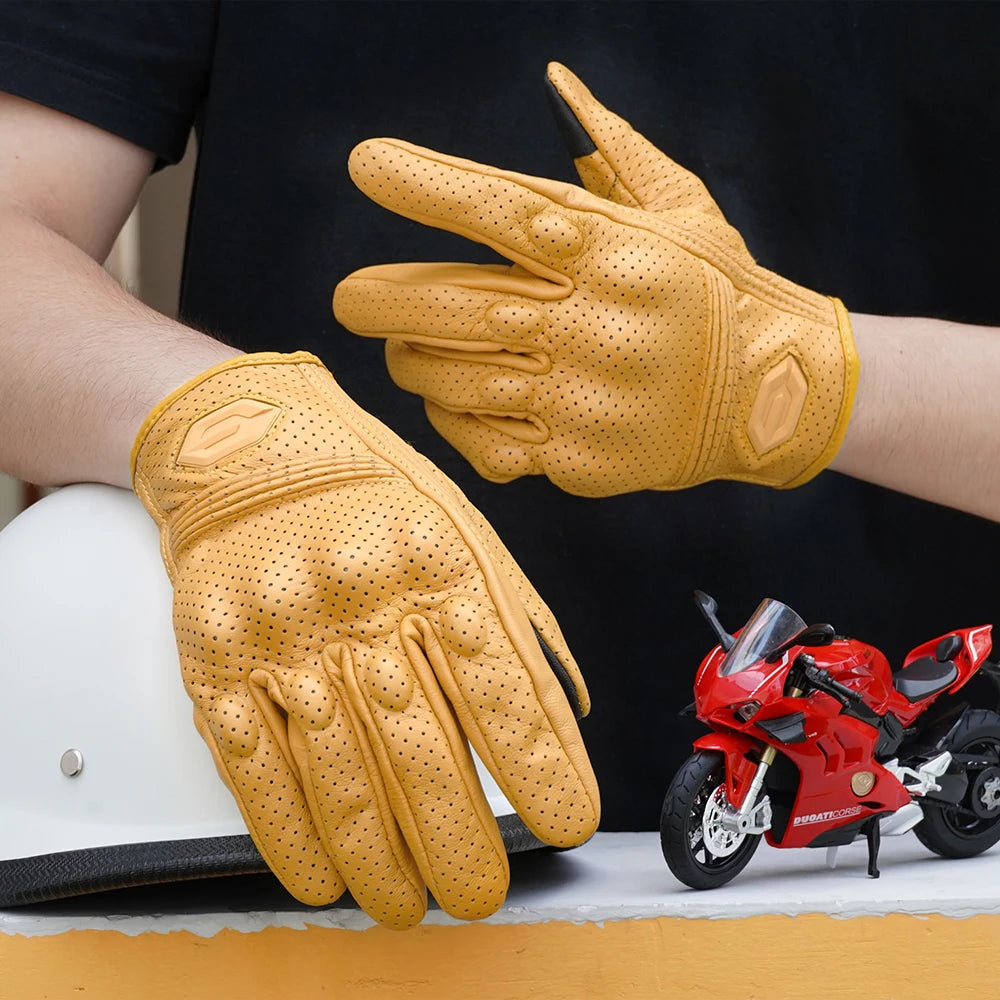 A pair of tan leather motorcycle riding gloves are shown on a person's hand and resting near a red motorcycle.