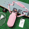 Botella de agua aislada rosa con funda y correa sobre césped verde junto a un smartphone blanco y una malla metálica