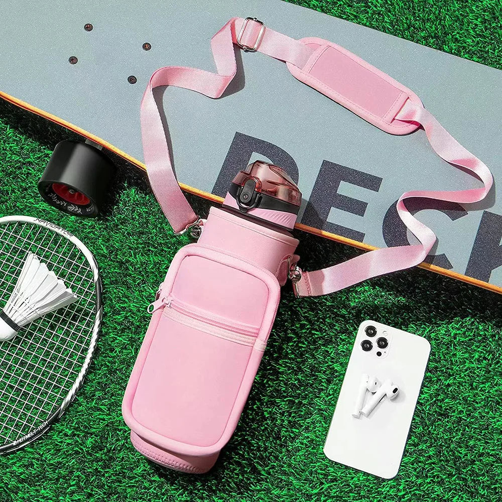 Botella de agua aislada rosa con funda y correa sobre césped verde junto a un smartphone blanco y una malla metálica