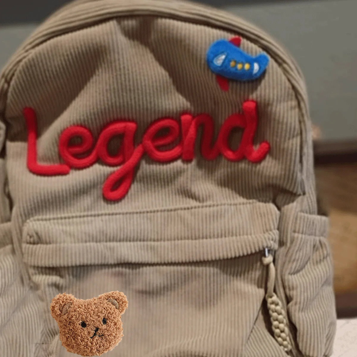 Helle braune Cordhosen-Rucksack mit der Stickerei "Legend" und einem kleinen blauen Vogelanhänger.