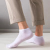 Ein Paar hellbeige Hosen und weiße Knöchelsocken an den Beinen einer Person.