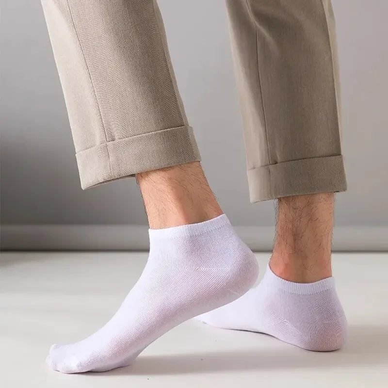 Ein Paar hellbeige Hosen und weiße Knöchelsocken an den Beinen einer Person.