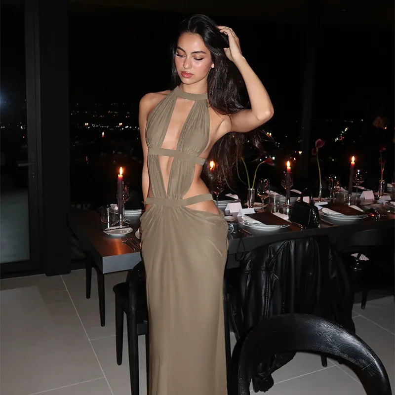 A model wearing an elegant, olive green maxi dress with a draped cut-out back, posing in a dimly lit restaurant setting.