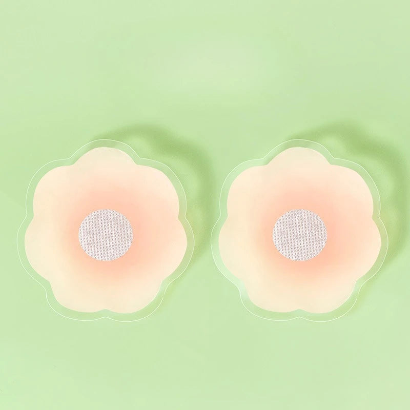Une paire de cache-sein en silicone réutilisable de couleur rose pâle est présentée sur un fond vert clair.