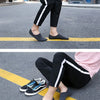 A person wearing black pants and gray socks is walking on asphalt with yellow lines visible.