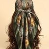 Pañuelo de satén verde oliva oscuro con estampado floral paisley bohemio, atado alrededor de cabello largo y castaño oscuro.