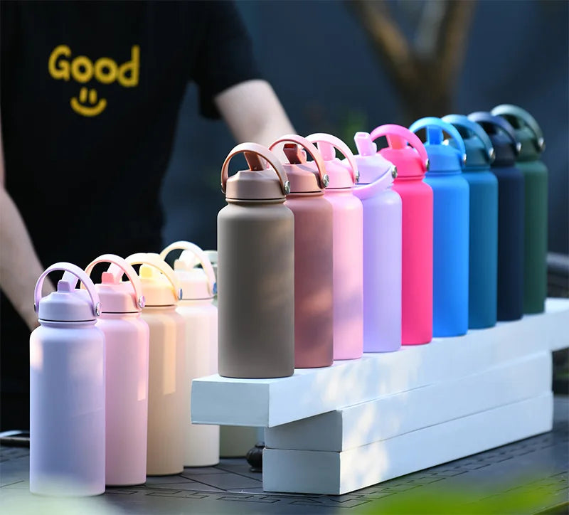 A row of pink and purple stainless steel vacuum flask water bottles with straws displayed on a white wooden surface.