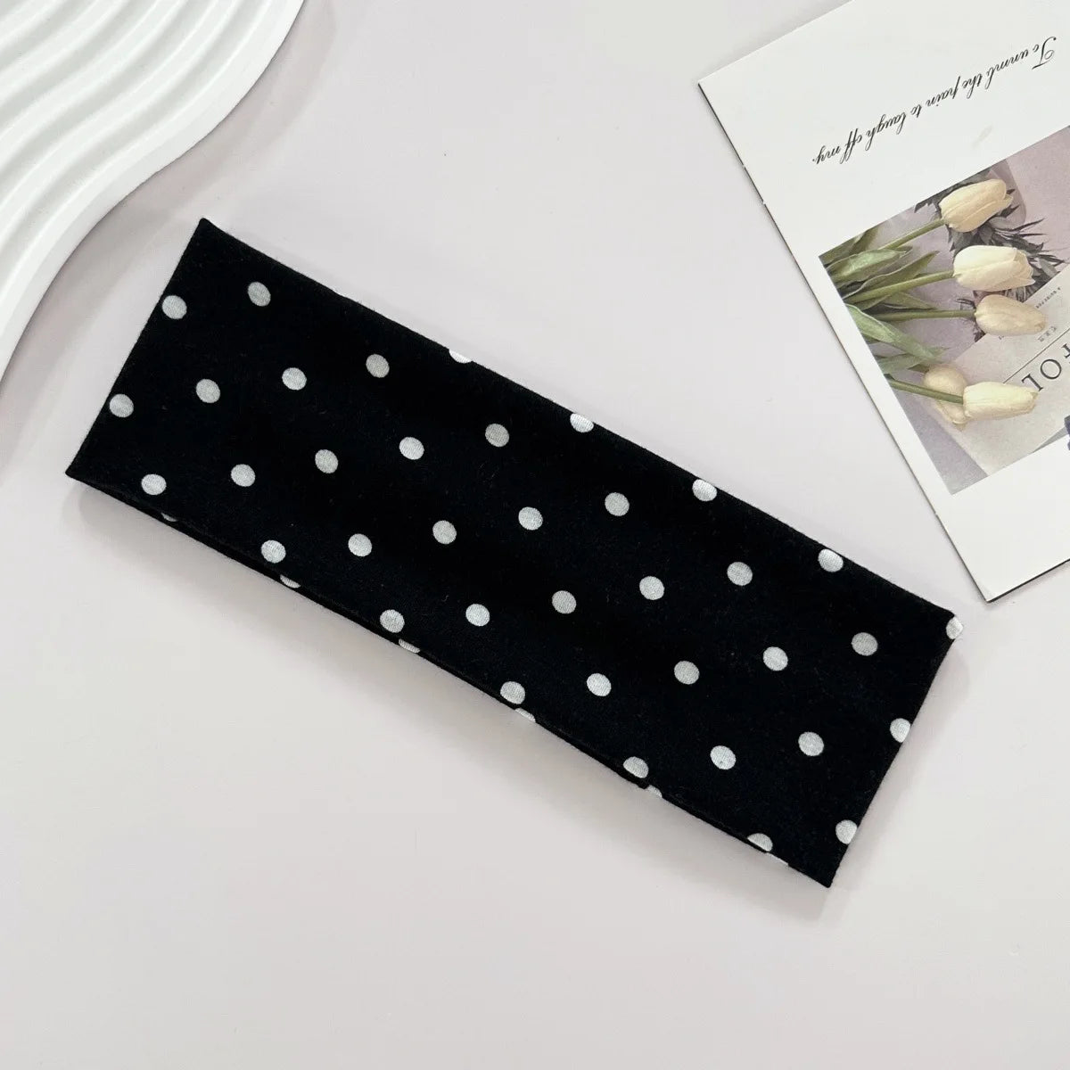 Bandeau de yoga élastique à pois noirs posé sur une surface blanche à côté d'un magazine.