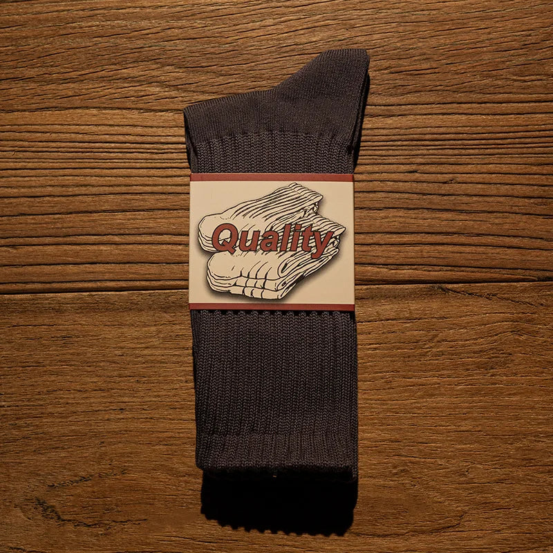 A pair of dark gray thick cotton tube socks with a white label featuring the word Quality.