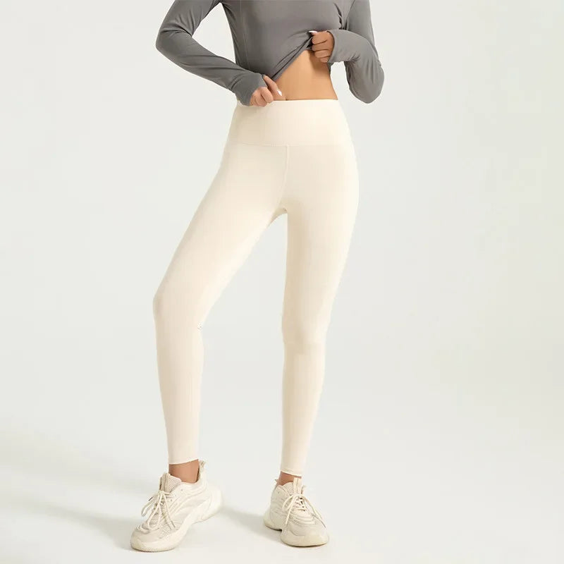 A model wearing beige seamless high-waist yoga leggings and a gray top, standing and posing.