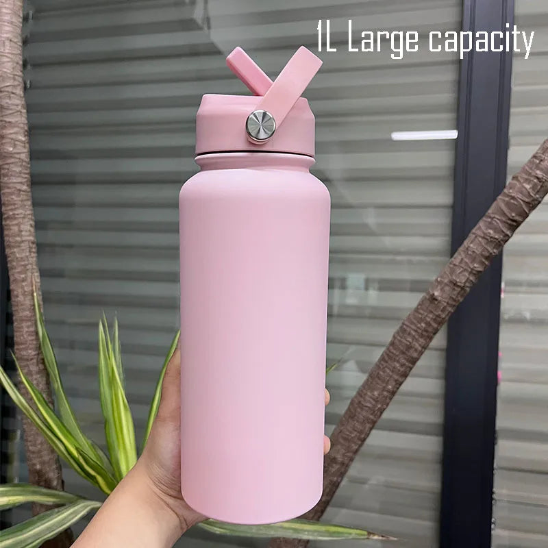 A pink stainless steel vacuum flask water bottle with a straw is held in a hand against a blurred background.