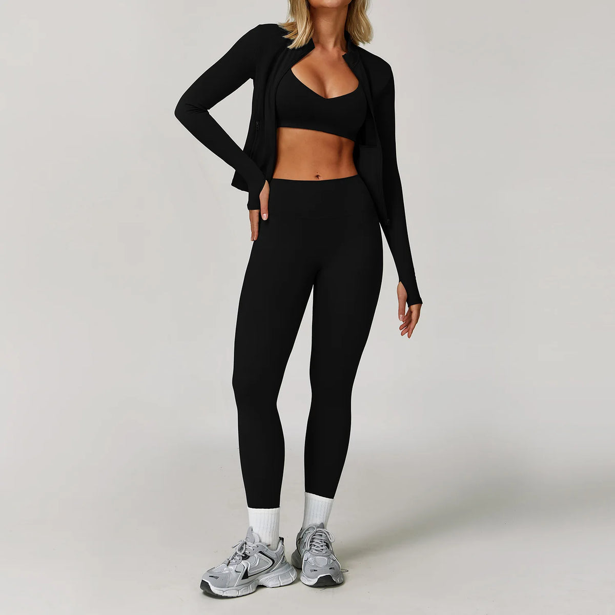 A woman models a black 3-piece yoga sports set consisting of a cropped top, leggings, and a long cardigan.