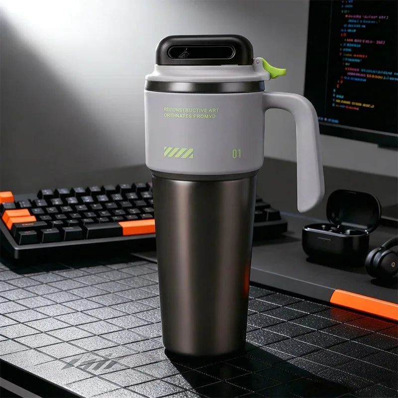 A matte gray insulated stainless steel tumbler with a handle and straw sits on a black desk mat.