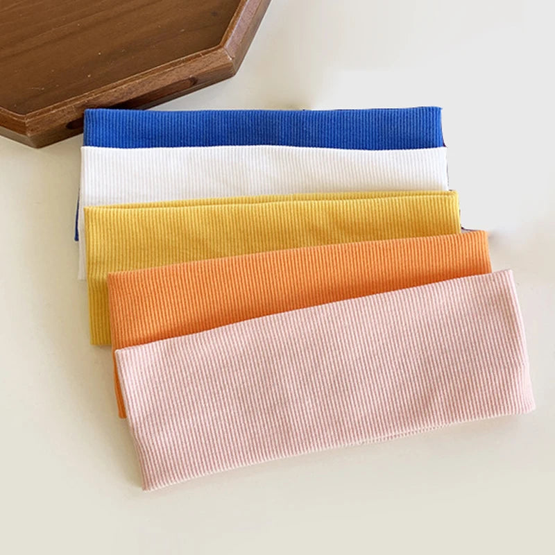 A stack of five elastic hairbands in blue, white, yellow, orange, and pink for fitness and yoga.