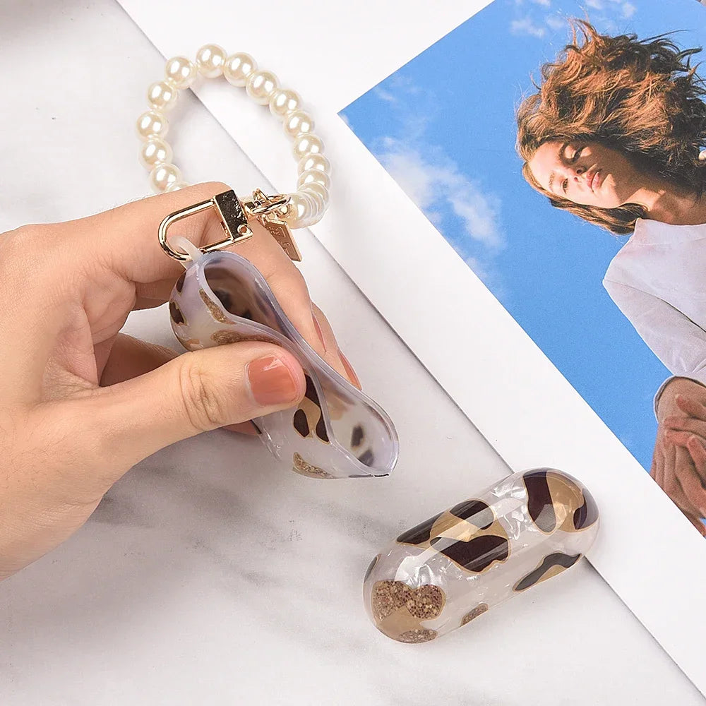 A hand holds a clear protective case with leopard print and an attached pearl necklace against a bright blue sky background.