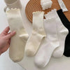 A hand holds a stack of white and cream cotton ruffle ankle socks on a wooden surface.