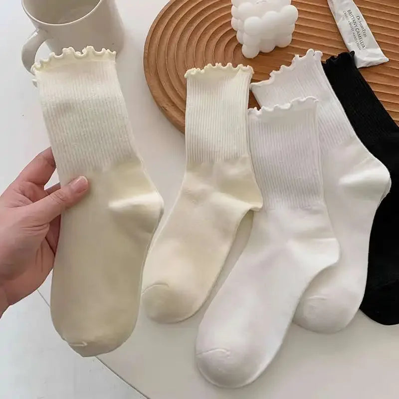 A hand holds a stack of white and cream cotton ruffle ankle socks on a wooden surface.