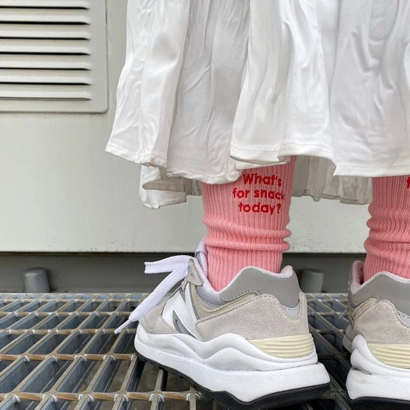 A close-up of a person wearing white ruffled clothing and pink socks with light gray sneakers.