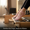 Pink crisscross strap yoga socks worn by a person on a wooden exercise bench.