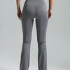 A person wearing high-waisted grey bootcut yoga pants and a black sports bra is standing against a light gray background.