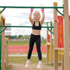 A young girl wearing a black sports outfit is holding onto a green bar during gymnastics practice.