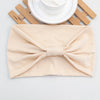 Beige weiche elastische breite Stirnband, gebunden mit Schleife, auf weißem Teller und Holzlatten.