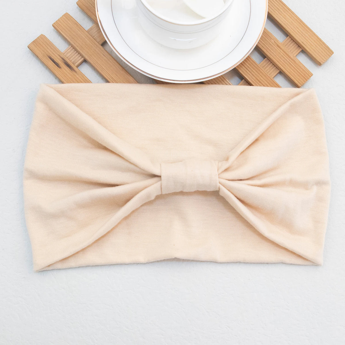 Beige weiche elastische breite Stirnband, gebunden mit Schleife, auf weißem Teller und Holzlatten.