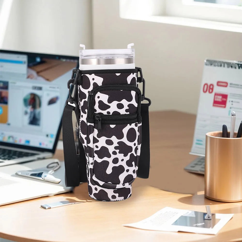 A black adjustable pouch carrier for a water bottle is shown on a wooden desk next to a laptop and papers.