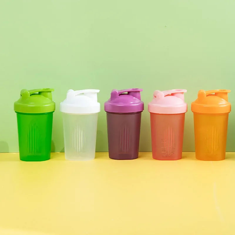 Five colorful leakproof protein shaker bottles in green, white, purple, pink, and orange lined up on a yellow surface.